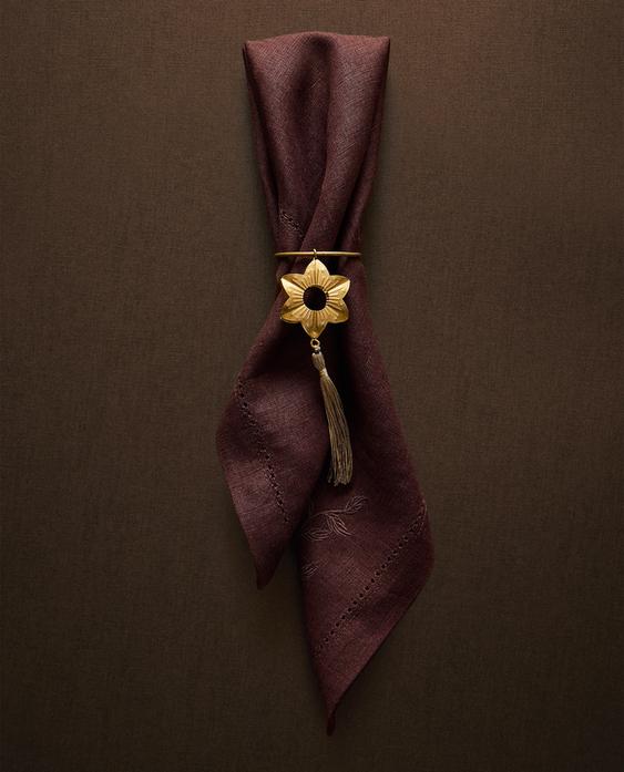 Zlata zvezdasta sponka za prtičke z resico, ki drži rjav prtiček z vezenjem listov.