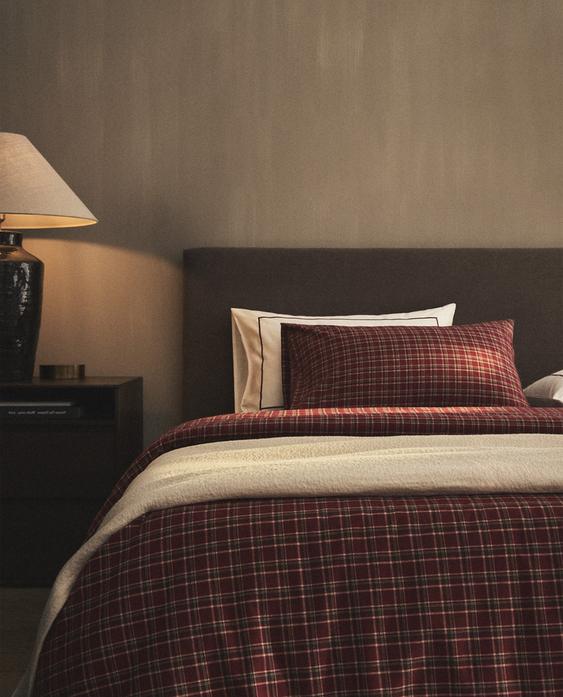 Sprednji pogled na rdečo prevleko za odejo s karirastim vzorcem in ujemajočo se blazino na postelji.