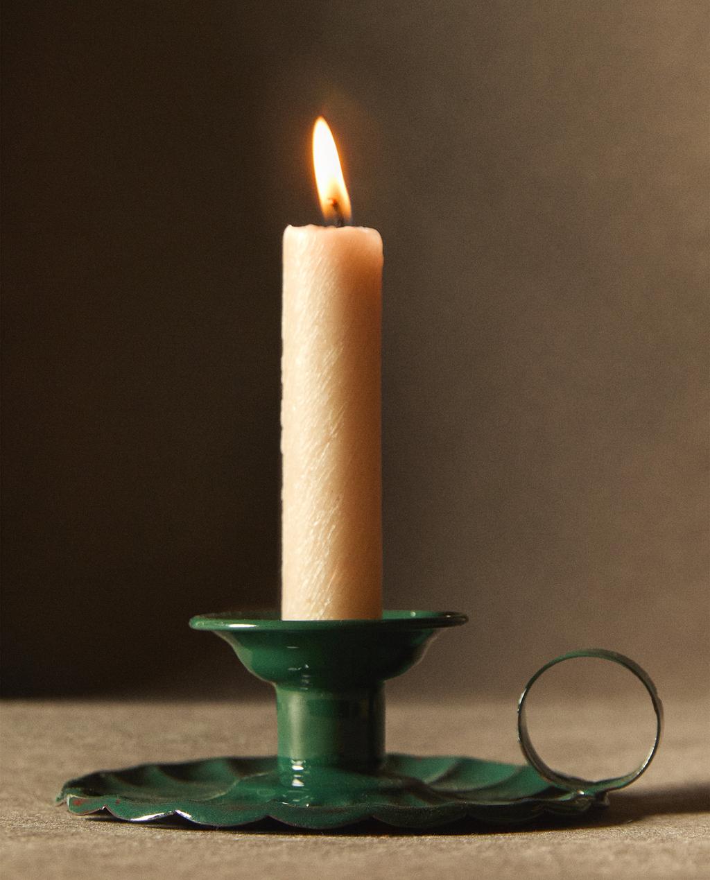Zeleni svečnik z valovitim krožnikom in okroglim ročajem, ki drži prižgano svečo.