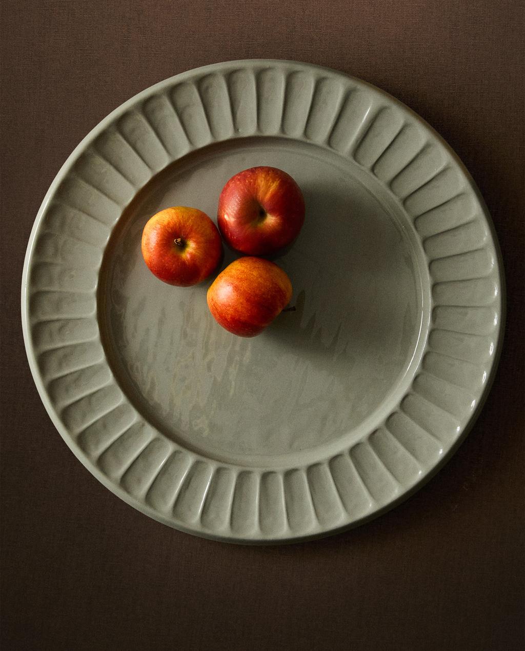 Pogled od zgoraj na zeleno okroglo posodo z nagubanim robom, okrašeno s tremi rdečimi jabolki na sredini.