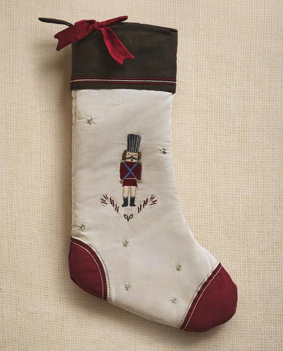 Večbarvni božični okras v obliki nogavice z vezenino hrestača in sladkornih palic, rdečimi detajli in okrasno pentljo.