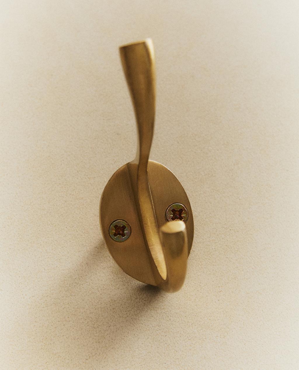 Detail of a gold wall hook with two visible screws