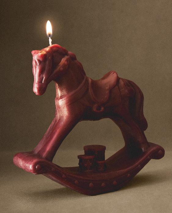 Upaljena crvena svijeća u obliku konjića za ljuljanje, dekorativni dizajnerski detalj na bazi.