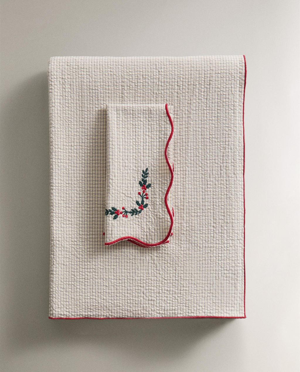 Pogled od spredaj na rdeč prt z rdečim robom in servieto z vezenjem listov in jagod.