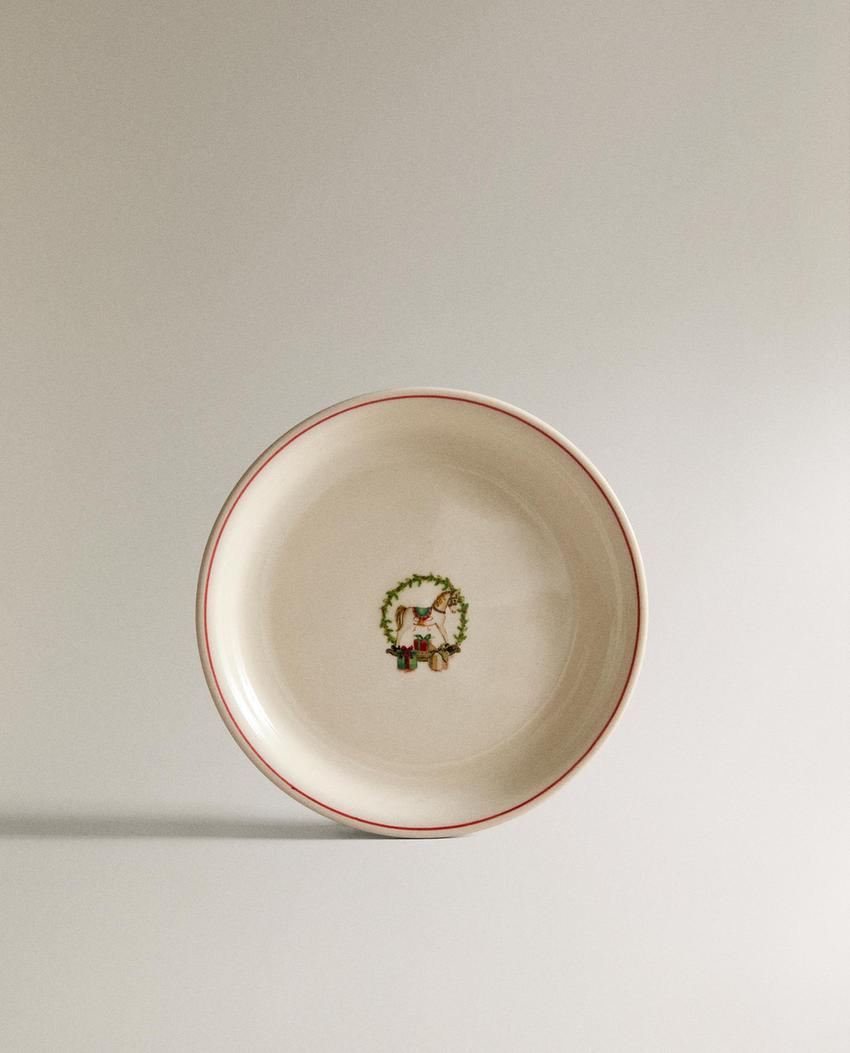 Sprednji pogled na bel krožnik z rdečim robom in osrednjim potiskom zelene kune z darili.